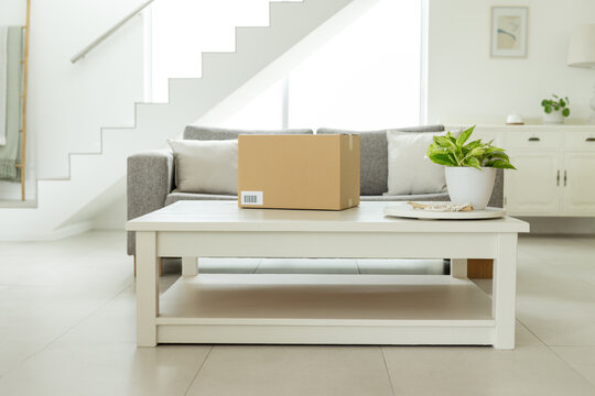 Small sealed cardboard box resting on white coffee table in bright living room, showing barcode