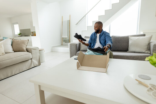African American adult man sitting in living room holding black shoes by shoebox, denim, copy space