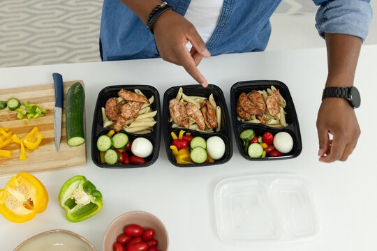 African American man pointing and arranging three black meal boxes with chicken on white countertop