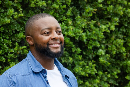 African American man standing posing by hedge wearing denim buttonup shirt white tee, copy space