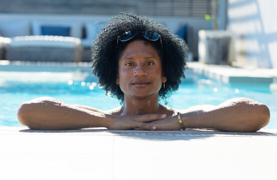 Adult man shirtless resting chest-deep in pool, leaning on deck, wearing sunglasses and bracelet