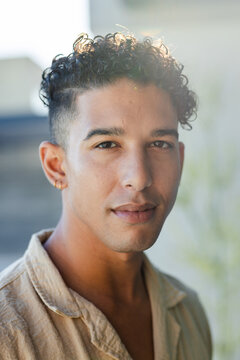Male posing for portrait, wearing beige linen shirt and gold hoop earring in courtyard