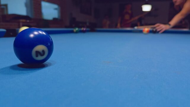 Close Up Of Blue Pool Ball On Felt With Woman Preparing Shot In Background Inside Dark Billiard Club
