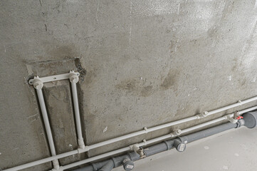 Concrete wall with mounted PVC water supply pipes and grey drainage pipes; features fittings,...