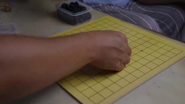 Close-up shot of the hands of a man and a woman, amateur Asian Go players, making moves on a board at home.