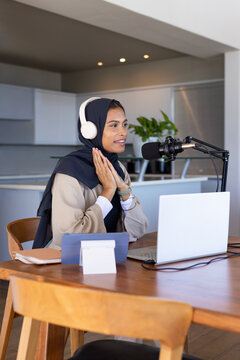 African American woman wearing dark hijab and tan blazer speaking into mic at kitchen dining table