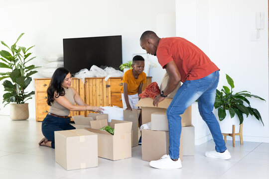 Diverse family packing moving boxes on living room floor with red textile and packing paper