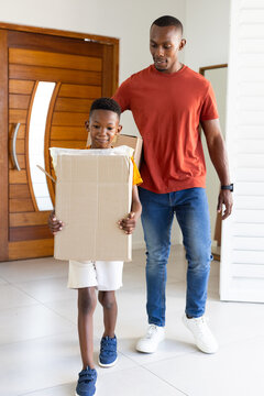 African American father and son carrying bubble-wrapped boxes at front door, son wearing yellow tee