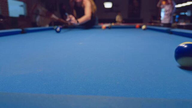 Close Up Of Blue And White Pool Ball On Felt While Woman Aims Cue In Background Inside Billiard Club