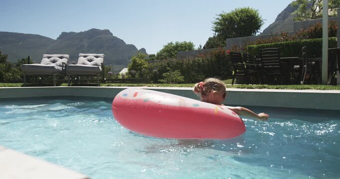 Youth female reaching with right arm, paddling and bringing pink donut float toward camera in pool
