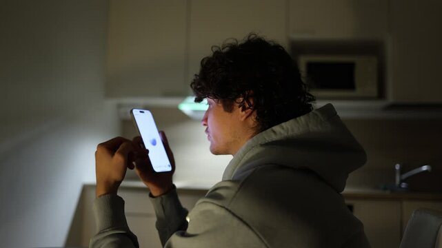Man sitting in dark kitchen at night using smartphone asking questions to chatgpt about daily routine and study tasks ai assistant helping at home