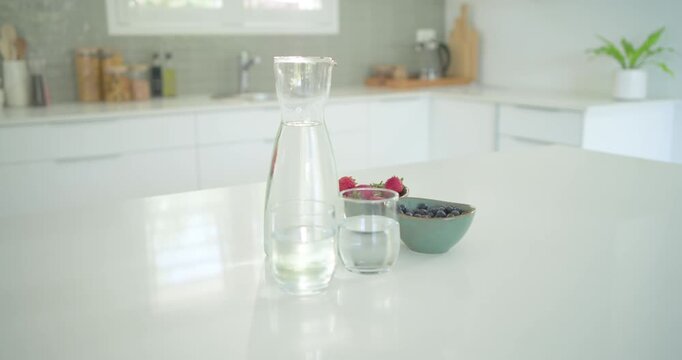 Camera is slowly pushing in to highlight glass carafe, glasses and blueberry bowl on countertop