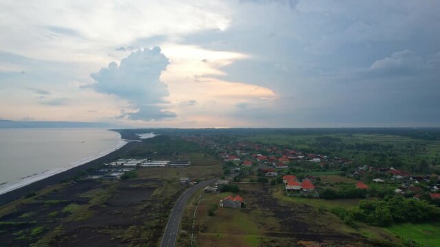 Aerial drone footage of the flat area in Jalan Lintas Selatan, nearby the coast of Lumajang regency, Java island, Indonesia, with many grass fields, local villages, at cloudy sunset time