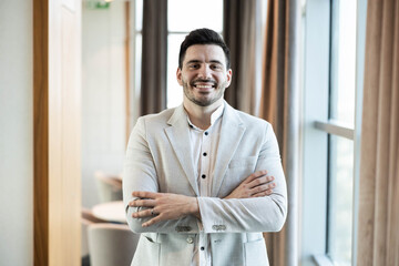 A confident man stands proudly with arms crossed, exuding professionalism in a bright space.