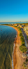 Aerial drone view of the tropical coastline of Castelhanos Beach in Anchieta, Esp&iacute;rito Santo, Brazil. Blue ocean waves meet golden sand and a scenic seaside town along the Atlantic coast.