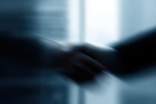 Business handshake captured from a distance, blurred office background, subject in the center-bottom, massive sky or ceiling space