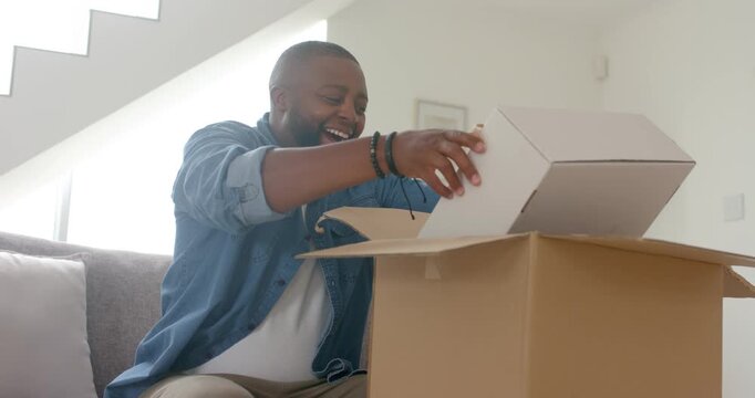 African American man sitting on sofa opening big package pulling white box checking items laughing