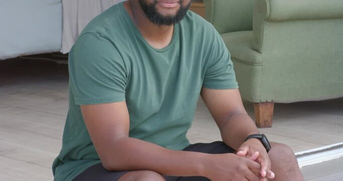African adult male sitting on threshold as camera pulling back, lifting gaze and smiling at camera