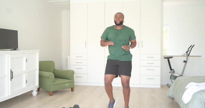 African man green-shirted starting with headset doing high knees into jumping jacks for cardio