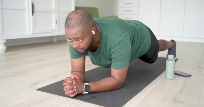 Adult African male tapping smartwatch timer, starting forearm plank at home holding mat