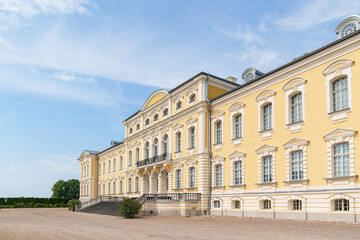 Fototapeta premium Grand yellow Rundale palace in Latvia stands under clear blue sky. Symmetrical windows line elegant stone facade. Wide staircase leads to grand entrance steps.