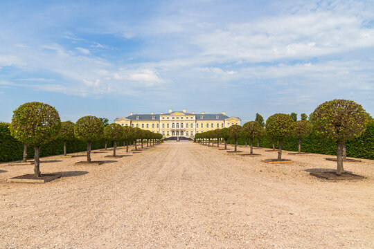 An alley with round trees and a sandy path leading to the large Rundale Castle in Latvia The sky is light blue with a few clouds
