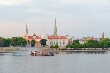 Obraz premium A pleasure boat sails along the Dune River in Riga, Latvia, with Riga Palace in the background The photo was taken at dusk
