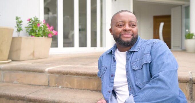 African man noticing camera turning and leaning on stoop clasping hands smiling with watch