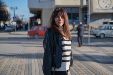 Obraz premium Young woman stands on a city street enjoying a day of exploration with people and cars around her during afternoon light
