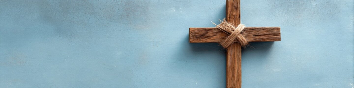 Horizontal wooden cross tied with twine on muted blue background panoramic banner simple rustic christian symbol