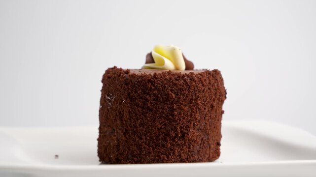 A chocolate cake with smooth frosting rotates slowly in a studio setup. The elegant dessert spins on a white background showcasing texture and decoration.