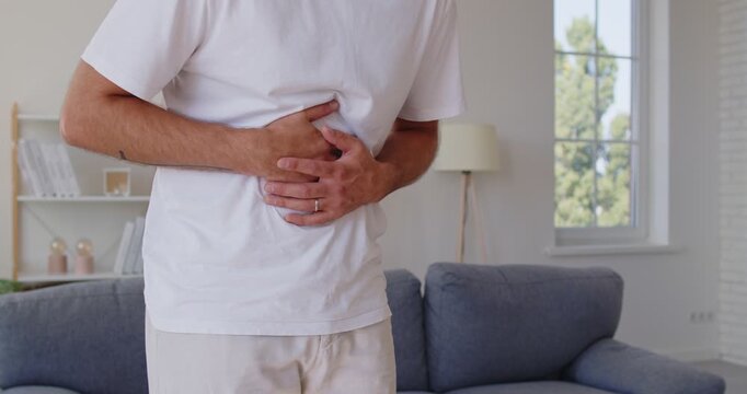 Sick man with bellyache and sharp abdominal pain holding hands on belly at home. Person showing stomach and bowel cramps, acid reflux, ache from indigestion, nausea of food poisoning or constipation