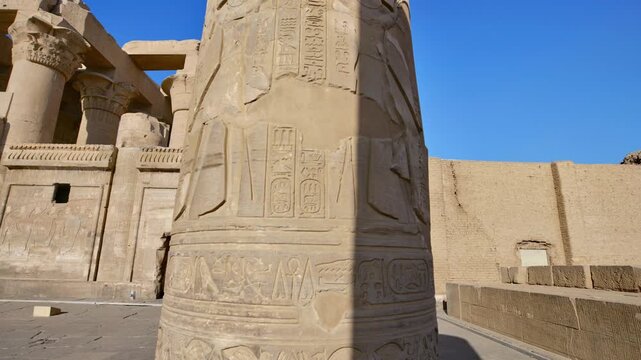 Kom Ombo temple columns with composite capitals and hieroglyphic carvings viewed from below against blue sky in Egypt, upward perspective of ancient sandstone architecture.
