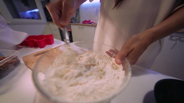 Closeup of hand mixing eggs and flour in glass bowl during baking