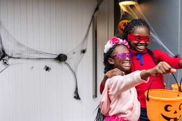 Naklejka premium Two African American girls posing at front door amid faux webs, holding pumpkin buckets, copy space