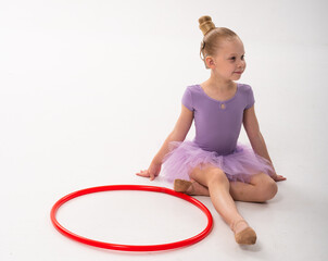 Naklejka premium Child ballerina with cochlear implant sitting near red hoop. Inclusive beauty, hearing technology, and self-confidence expressed through dance and childhood joy.