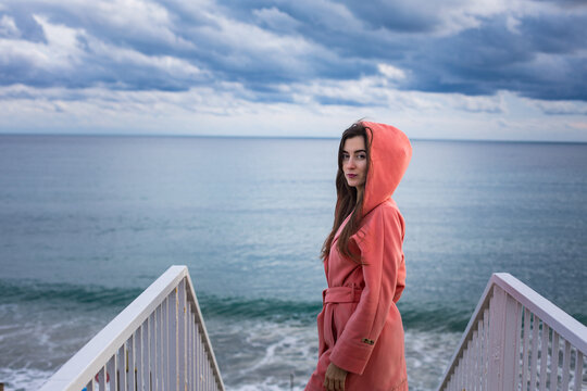 a girl in a coral coat against the backdrop of the sea in autumn