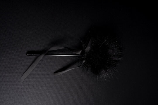 Fetish accessory with artificial fur tip on dark fabric background. Sensory tickler wand designed for gentle touches and tactile play, studio shot with copy space.