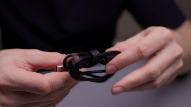 Hands untangling usb type-a and type-c plugs ready to connect devices, showing cable untangling and setup for charging and data transfer in dark studio setting, close-up, slow motion.