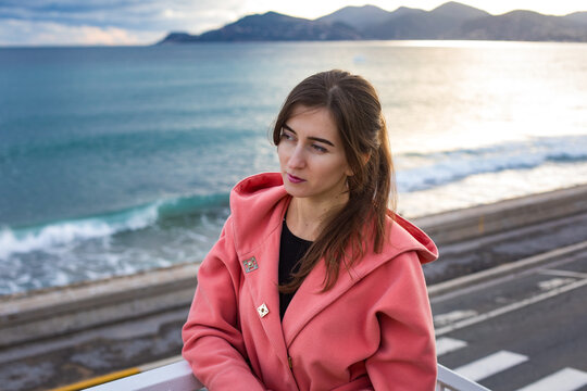 a girl in a coral coat against the backdrop of the sea in autumn