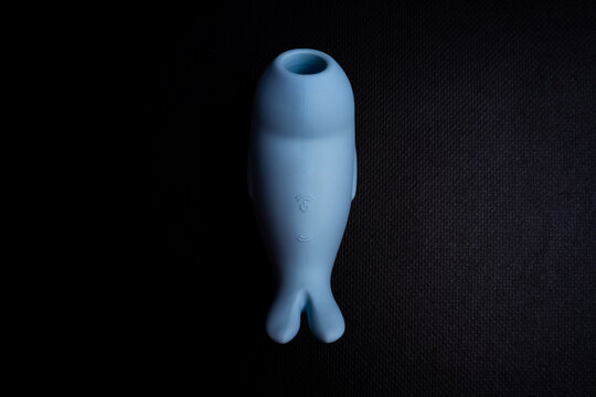 Blue silicone suction stimulator shaped like a seal, placed on dark textured background under studio lighting.