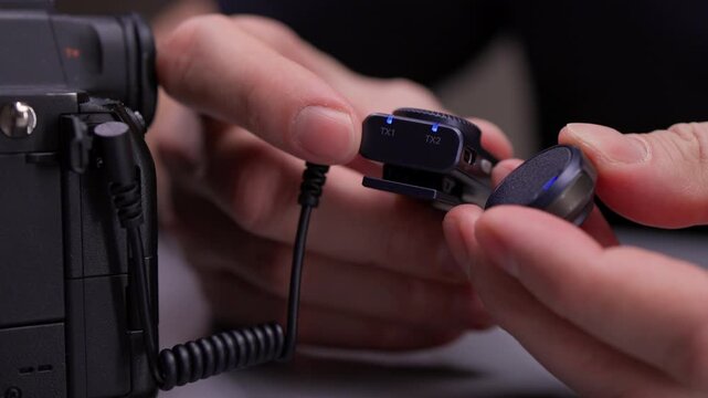 Close-up view of videographer hands setting up and synchronizing wireless lapel microphone system, connecting receiver to digital camera for professional audio recording. Shooting in slow motion.