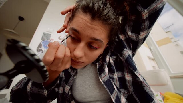 Woman practices eyeliner drawing in relaxed setting with mirror focus