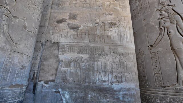 Kom Ombo temple columns with composite capitals and hieroglyphic carvings viewed from below against blue sky in Egypt, upward perspective of ancient sandstone architecture.