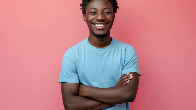 Young man smiles warmly against vibrant pink background. He wears a simple blue t-shirt, arms crossed confidently. His joyful expression radiates friendliness and approachability