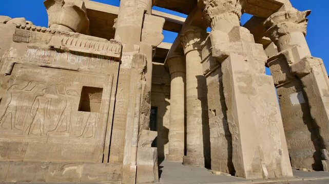 Kom Ombo temple ruins with double columns and composite capitals against clear blue sky in Egypt, ancient Ptolemaic architecture dedicated to Sobek and Horus with damaged walls.