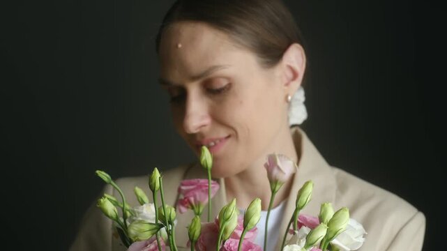 Beautiful elegant woman with closed eyes enjoying the delicate fragrance of a fresh bouquet of pink and white eustoma flowers, smelling the blooms with a gentle and happy smile