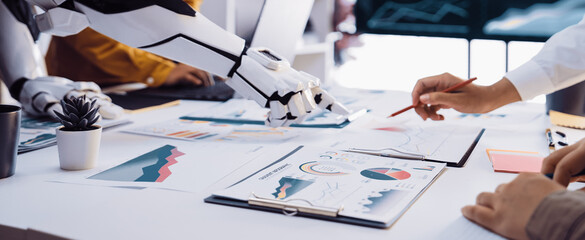 Fototapeta premium A robotic arm collaborates with humans in a modern office, analyzing data through charts and graphs, showcasing the integration of technology in business strategies.Noogenesis