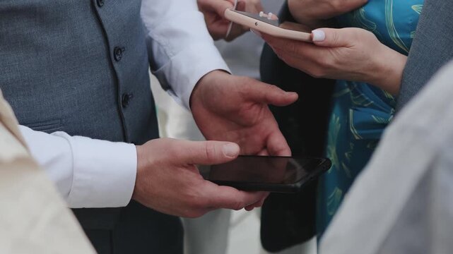 People scanning QR code on smartphones. Wedding registration with Caucasian guests exchanging smartphones and invitations at the entrance to the ceremony, groom. 