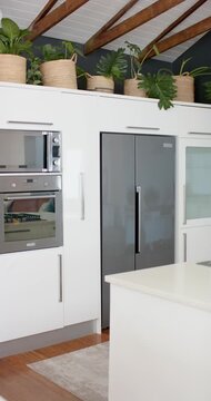 Vertical video: Camera is panning right revealing cabinets and stainless fridge to show island
